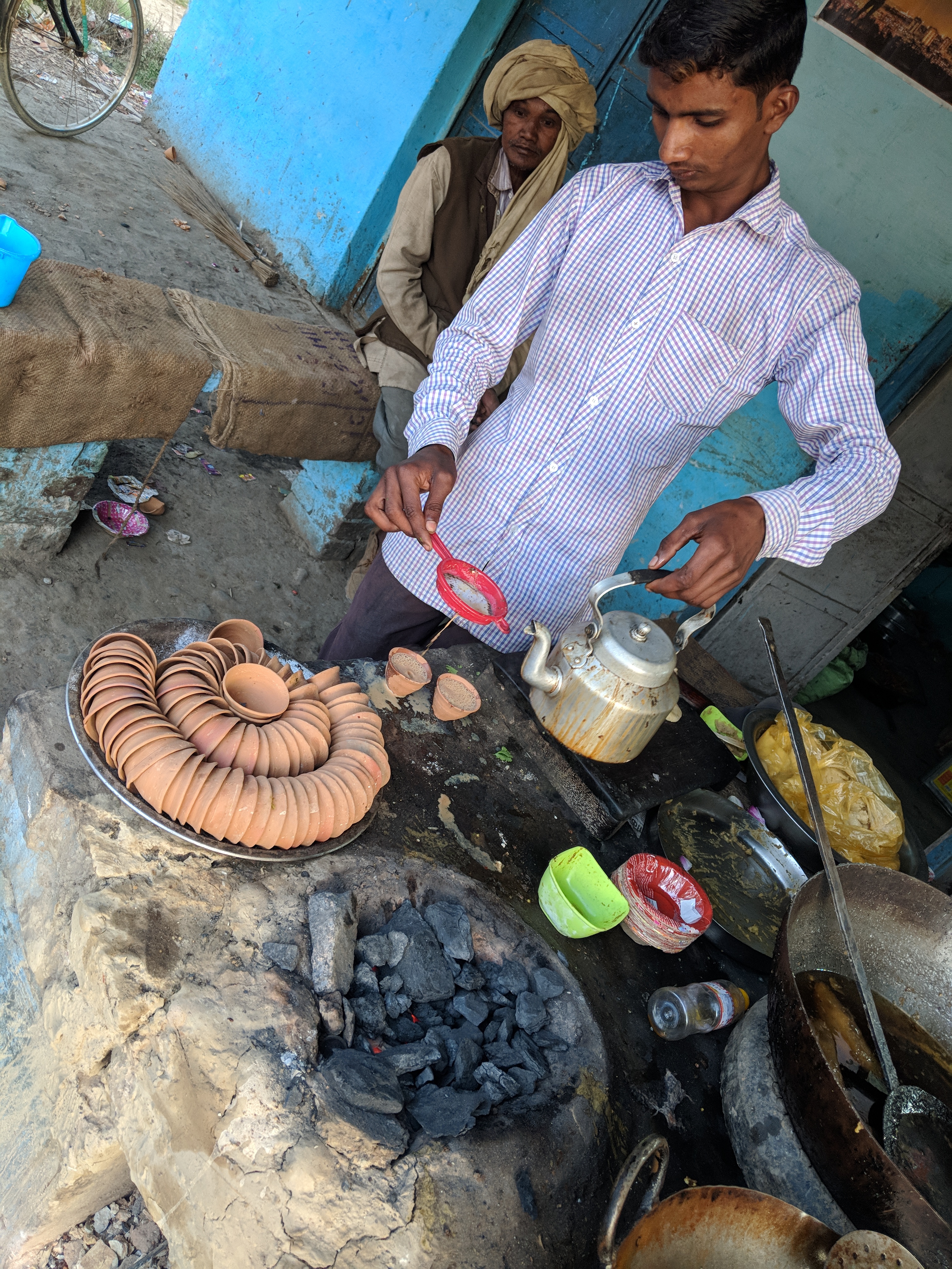 A Tea shop iwth tea being served in disposable mud cups. Tea is prepared on a coal stove