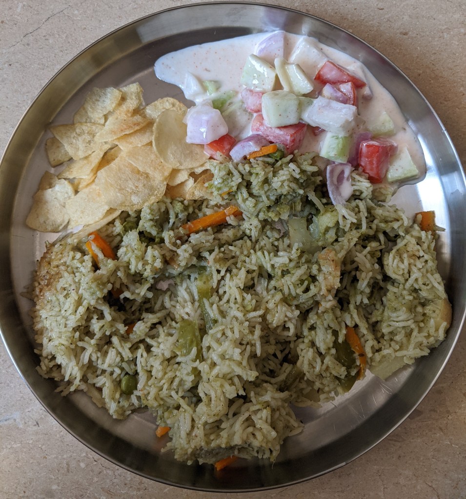 A plate of south indian pulav made with coconut and coriander ground with spices and lots of vegetables along with raita