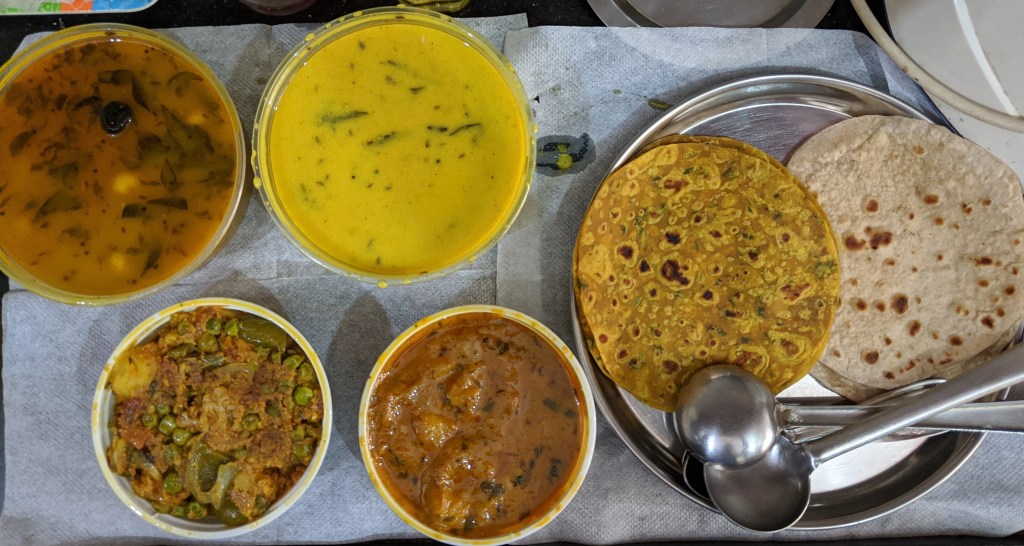 Packed lunch from a Gujarati caterer - Cauliflower capsicum and peas curry, Aloo rassawala, Marwadi kadi, Gujarati dal. Methi thepla and Chapatis